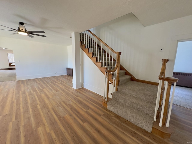 stairway featuring radiator heating unit, wood finished floors, arched walkways, and baseboards