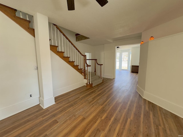 unfurnished room featuring baseboards, wood finished floors, and stairs