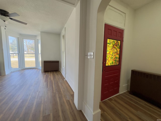 entrance foyer with wood finished floors, radiator heating unit, arched walkways, ceiling fan, and a textured ceiling