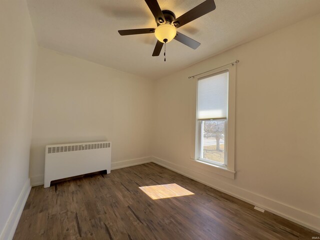 empty room with dark wood-style floors, ceiling fan, radiator heating unit, and baseboards