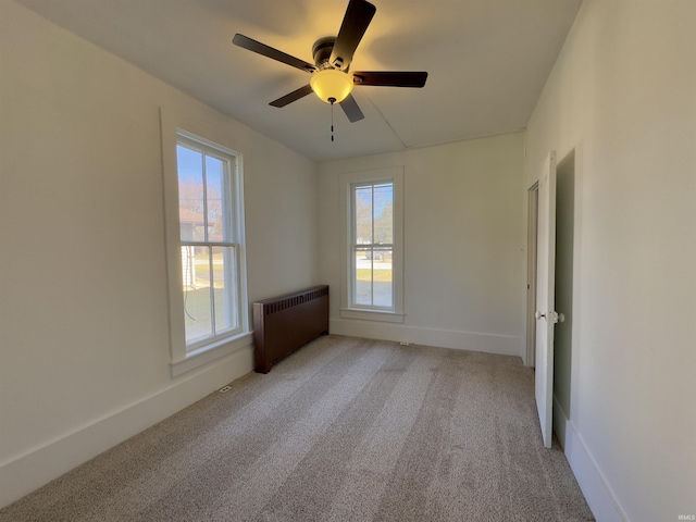 unfurnished room featuring light colored carpet, baseboards, radiator, and ceiling fan