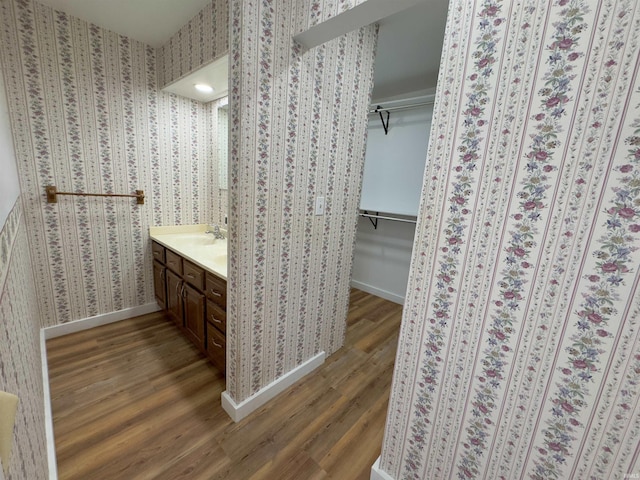 full bathroom featuring wallpapered walls, vanity, a spacious closet, and wood finished floors