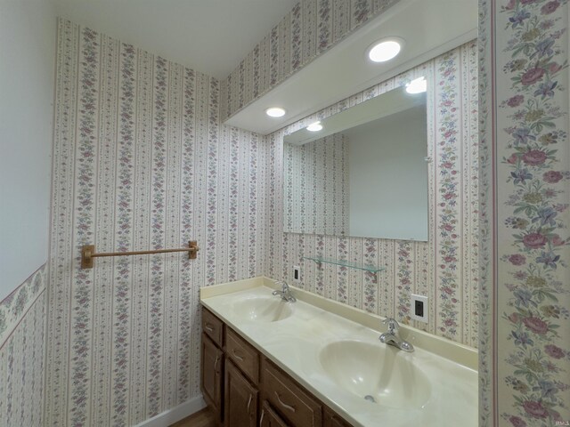 full bathroom featuring wallpapered walls, double vanity, and a sink