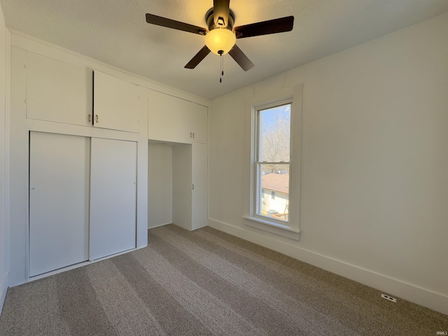 unfurnished bedroom with a closet, baseboards, light colored carpet, and a ceiling fan