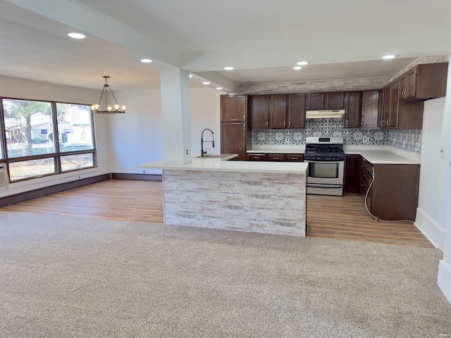 kitchen with light carpet, under cabinet range hood, stainless steel range with gas cooktop, decorative backsplash, and dark brown cabinets