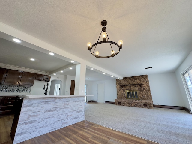 kitchen with arched walkways, dark brown cabinetry, an inviting chandelier, a fireplace, and light countertops