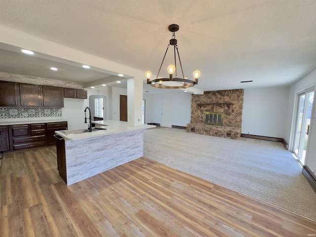 kitchen featuring dark brown cabinetry, open floor plan, light countertops, a fireplace, and a sink