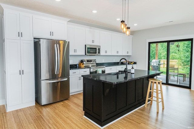 kitchen featuring an island with sink, light wood-type flooring, appliances with stainless steel finishes, white cabinets, and a sink