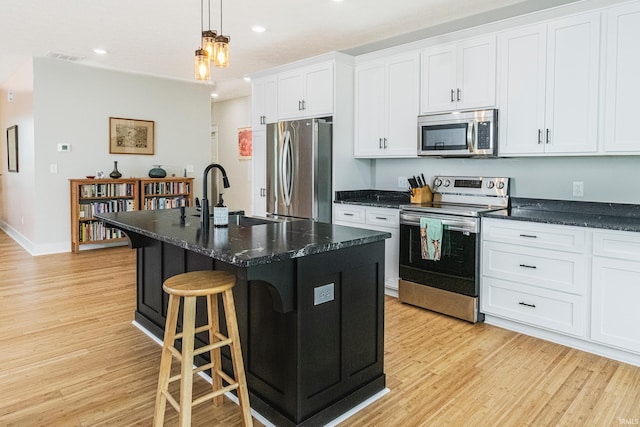 kitchen with a center island with sink, light wood-type flooring, appliances with stainless steel finishes, a kitchen breakfast bar, and a sink