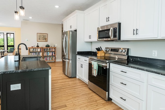 kitchen featuring an island with sink, light wood-type flooring, appliances with stainless steel finishes, white cabinets, and a sink