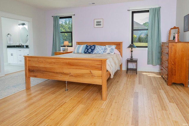 bedroom featuring baseboards, visible vents, light wood finished floors, a sink, and connected bathroom