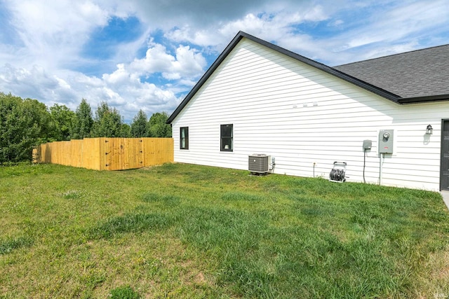 view of property exterior with central air condition unit, a lawn, a shingled roof, and fence