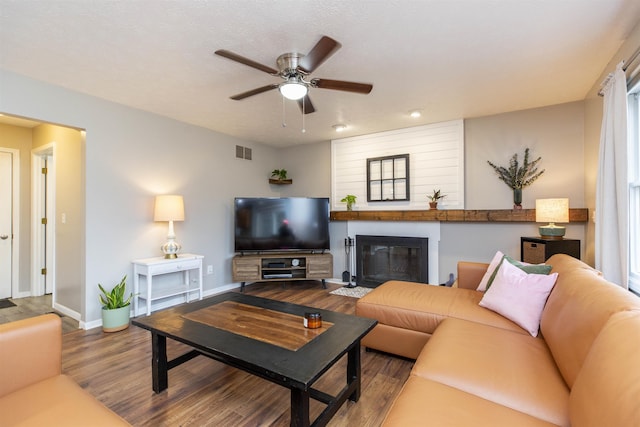 living area with visible vents, baseboards, wood finished floors, a glass covered fireplace, and a ceiling fan