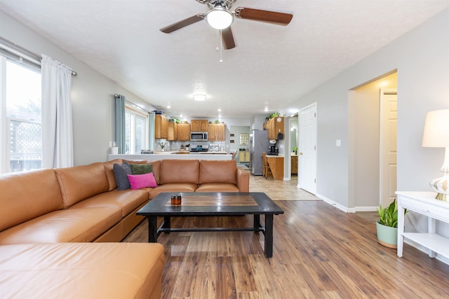 living room with baseboards, a textured ceiling, a ceiling fan, and light wood finished floors