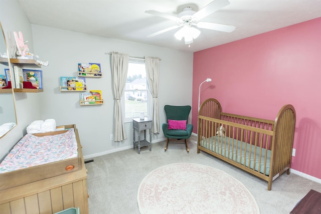 carpeted bedroom with a crib, visible vents, baseboards, and ceiling fan