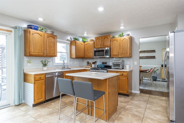 kitchen with a sink, light countertops, appliances with stainless steel finishes, a kitchen bar, and a center island