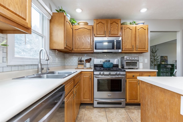 kitchen with backsplash, appliances with stainless steel finishes, light countertops, and a sink