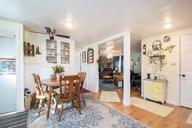 dining area with light wood-style floors, wainscoting, and a ceiling fan