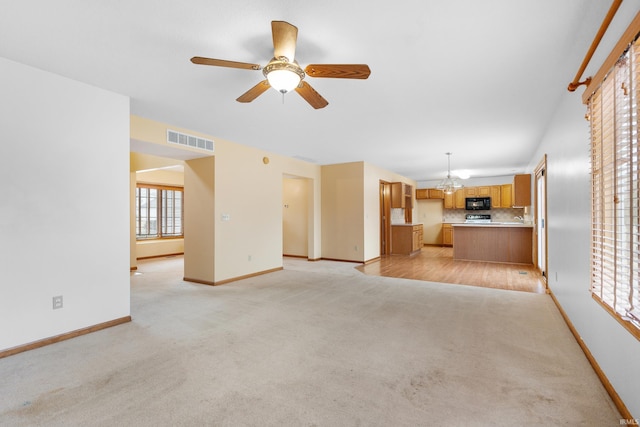 unfurnished living room with ceiling fan with notable chandelier, baseboards, visible vents, and light carpet