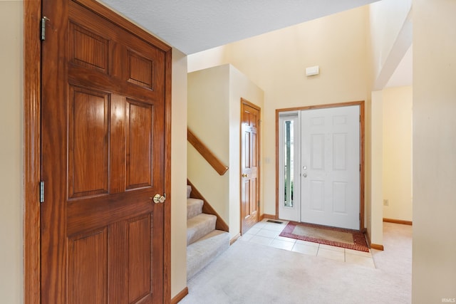 foyer entrance featuring a textured ceiling, light tile patterned floors, baseboards, light colored carpet, and stairs