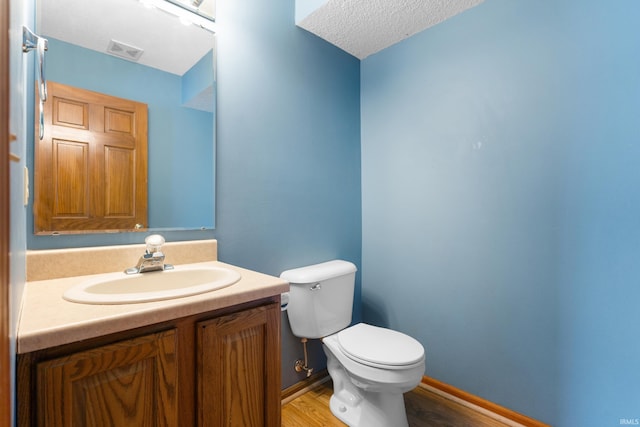 half bathroom with vanity, wood finished floors, baseboards, visible vents, and toilet