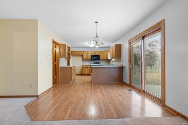 kitchen featuring a peninsula, stove, light countertops, black microwave, and backsplash