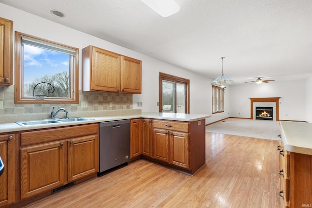 kitchen featuring visible vents, a sink, a warm lit fireplace, a peninsula, and dishwasher