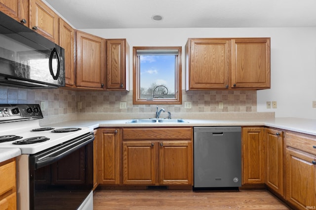 kitchen featuring black microwave, dishwasher, electric range oven, light wood-style floors, and a sink