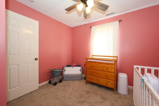 bedroom featuring visible vents, a crib, baseboards, carpet floors, and a ceiling fan