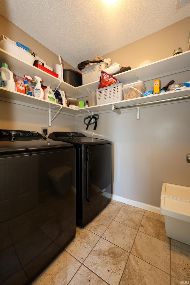 laundry room with washer and clothes dryer, a textured ceiling, light tile patterned flooring, baseboards, and laundry area