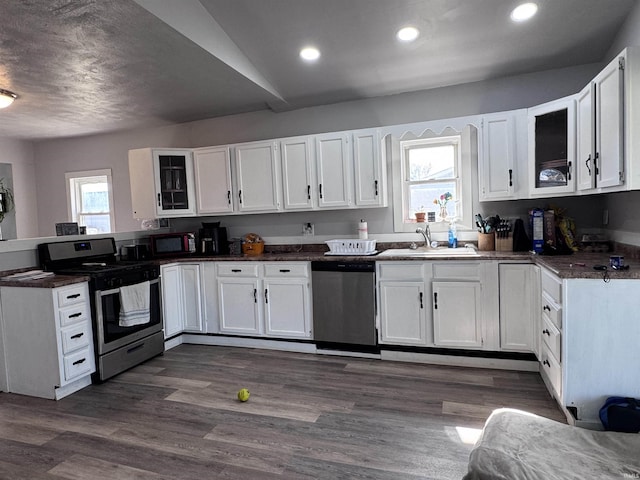 kitchen with a sink, white cabinetry, stainless steel appliances, a peninsula, and glass insert cabinets