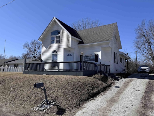 view of front of home with a wooden deck, fence, driveway, and a shingled roof