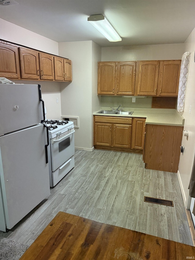 kitchen with visible vents, white appliances, light wood-style floors, and brown cabinets