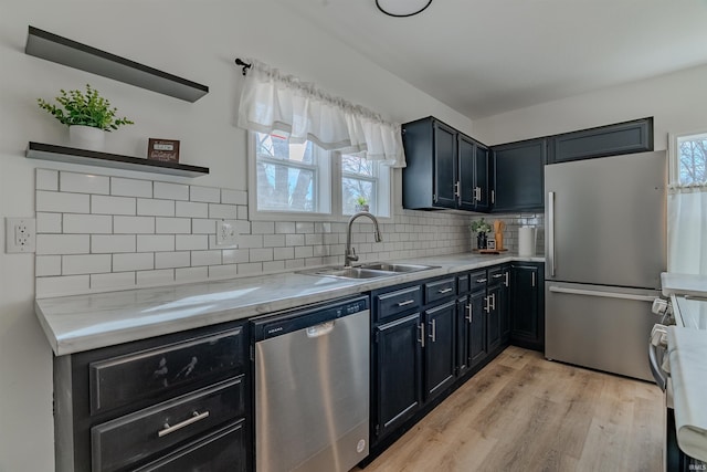 kitchen featuring a sink, backsplash, light wood-type flooring, stainless steel appliances, and open shelves