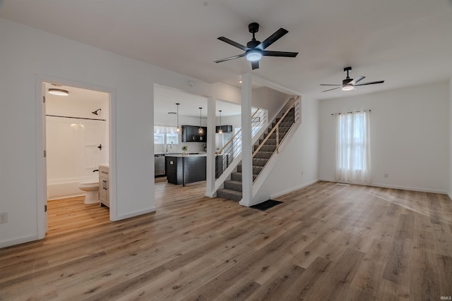 unfurnished living room with light wood-type flooring, visible vents, a sink, stairway, and baseboards