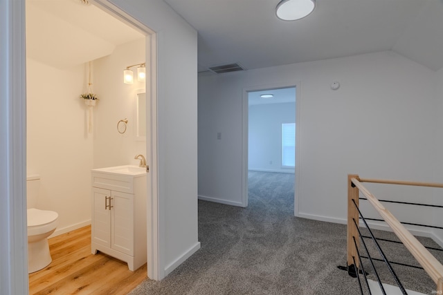 corridor featuring a sink, visible vents, baseboards, and an upstairs landing