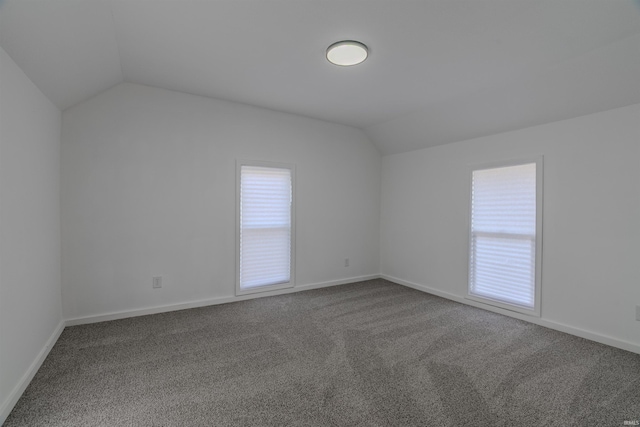 carpeted spare room featuring vaulted ceiling and baseboards