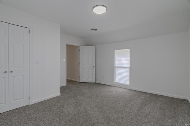 unfurnished bedroom with visible vents, lofted ceiling, a closet, carpet, and baseboards