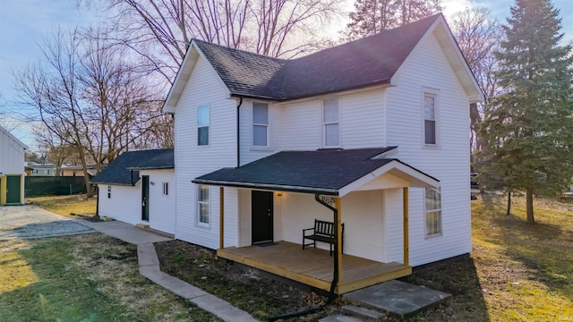 view of front facade with roof with shingles, covered porch, and a front yard