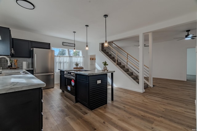 kitchen with light wood finished floors, tasteful backsplash, a sink, stainless steel appliances, and dark cabinets