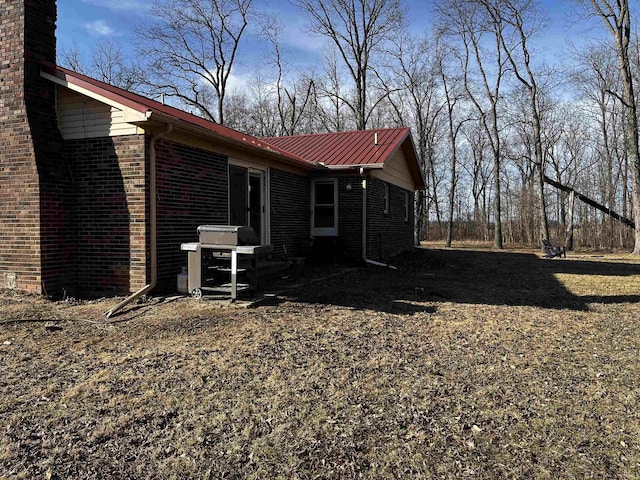 view of side of property featuring metal roof, brick siding, and a chimney