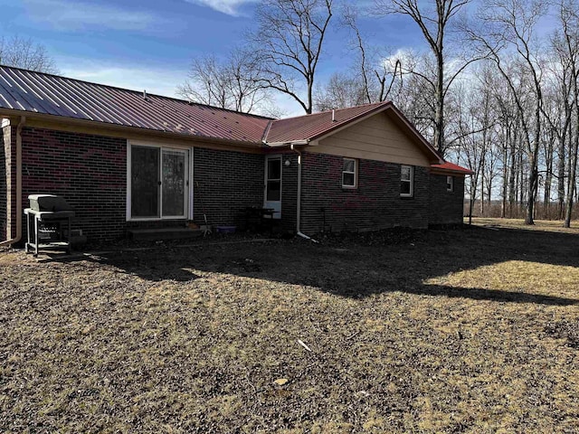 rear view of house featuring brick siding, entry steps, and metal roof