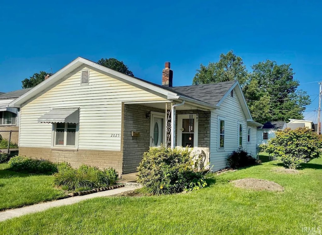 view of front facade with brick siding, a front yard, a chimney, and a shingled roof