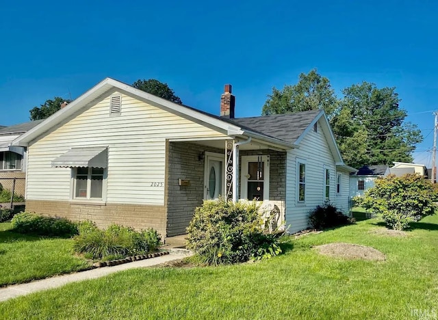 view of front facade with brick siding, a front yard, a chimney, and a shingled roof