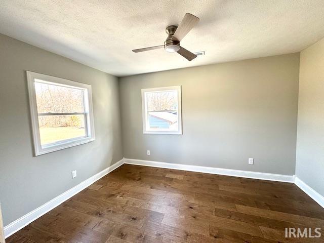 unfurnished room with a ceiling fan, visible vents, baseboards, dark wood-type flooring, and a textured ceiling