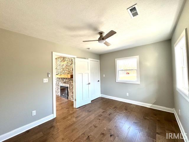 unfurnished bedroom with dark wood-style floors, visible vents, baseboards, a fireplace, and a textured ceiling