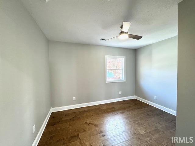 spare room with visible vents, baseboards, dark wood-type flooring, and ceiling fan