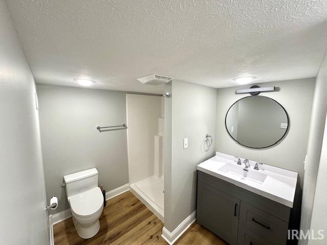 bathroom featuring a shower stall, baseboards, toilet, wood finished floors, and vanity