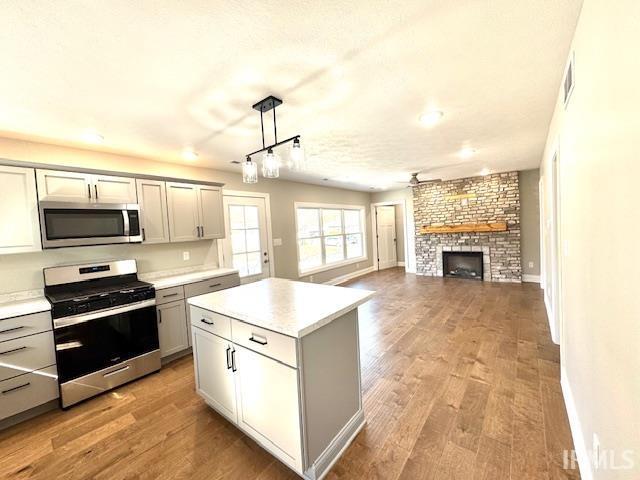 kitchen with appliances with stainless steel finishes, a fireplace, gray cabinetry, and light wood finished floors