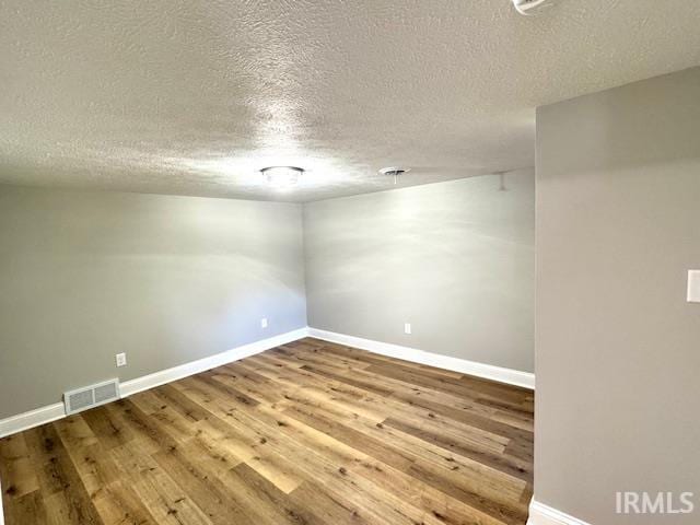 spare room with visible vents, a textured ceiling, baseboards, and wood finished floors